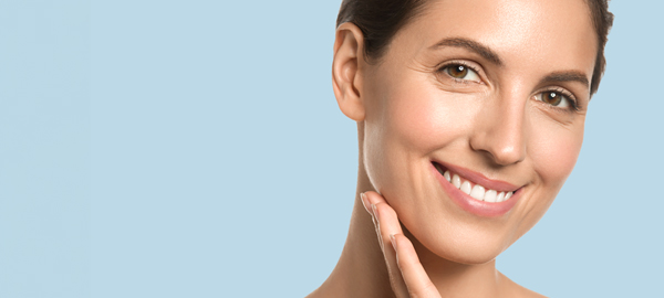 Mujer joven con piel saludable sonriendo y tocándose la cara